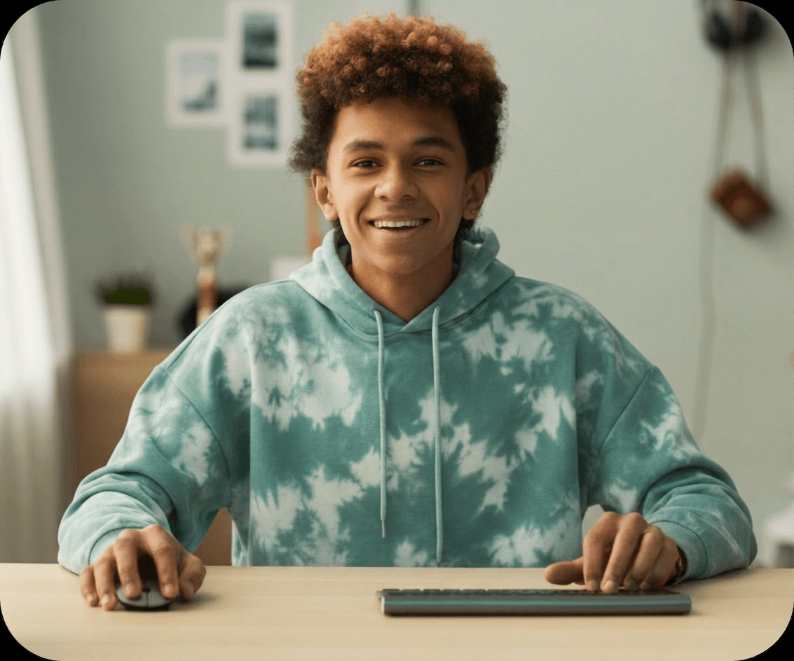 Teenage student in a tie-dye hoodie smiling while working at a computer